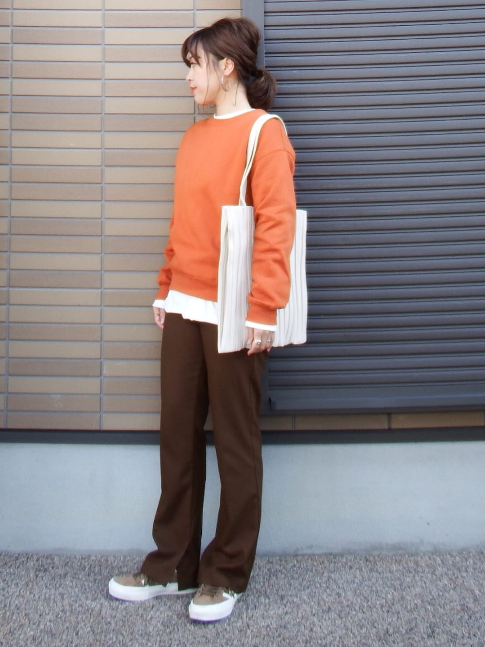 オレンジ系のトップス、ブラウン系のスラックス、ホワイト系のトートバッグを着用したレディースの冬コーディネートの1枚目の写真