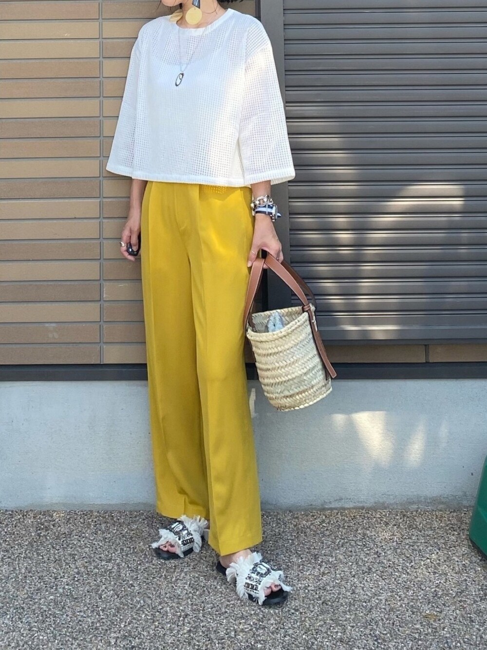 イエロー系のスラックス、ホワイト系のTシャツ/カットソー、ベージュ系のかごバッグを着用したレディースの夏コーディネートの1枚目の写真