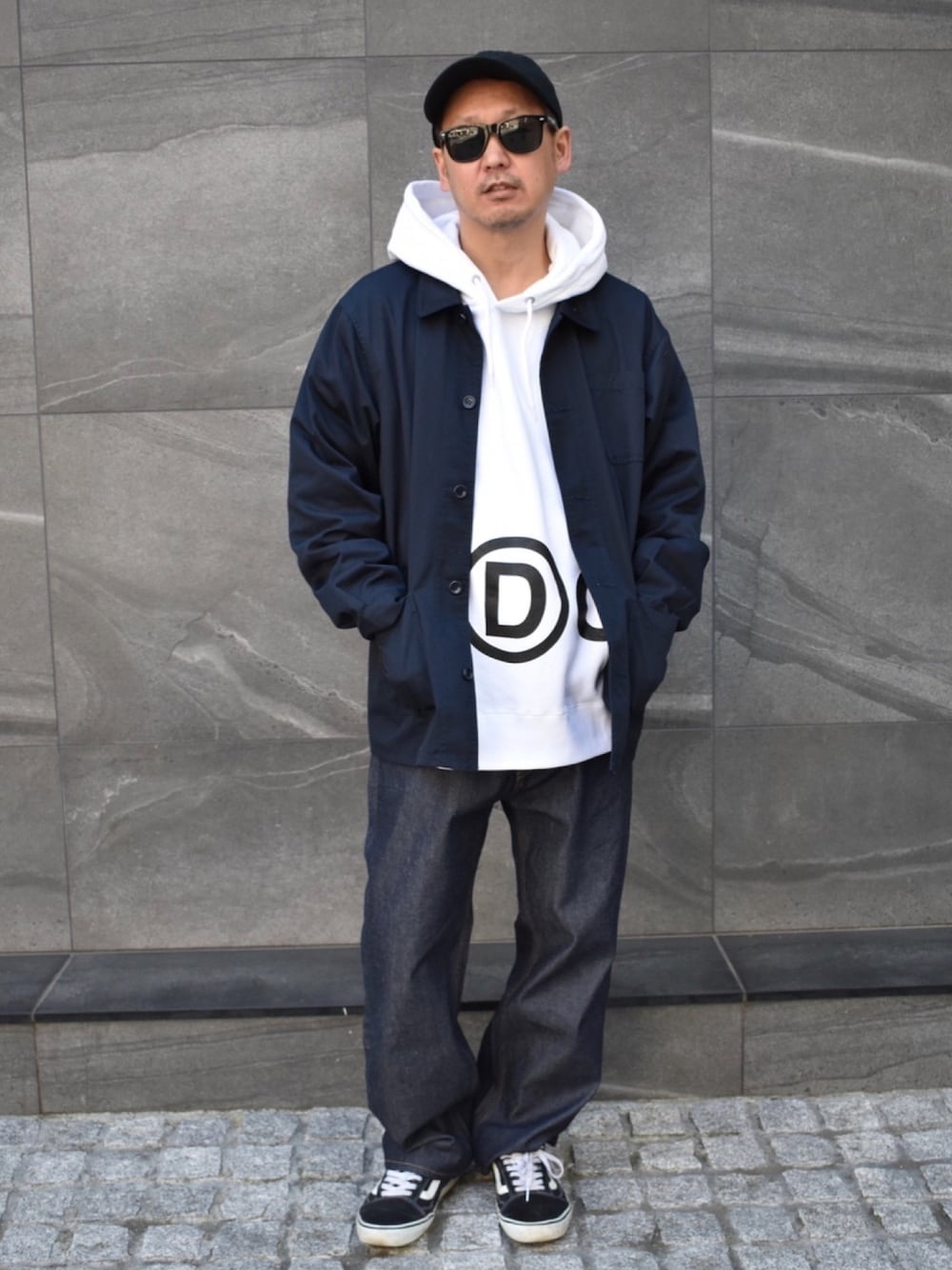 ブラック系のスニーカー、ブルー系のデニムパンツ、ホワイト系のパーカーを着用したメンズの春コーディネートの1枚目の写真