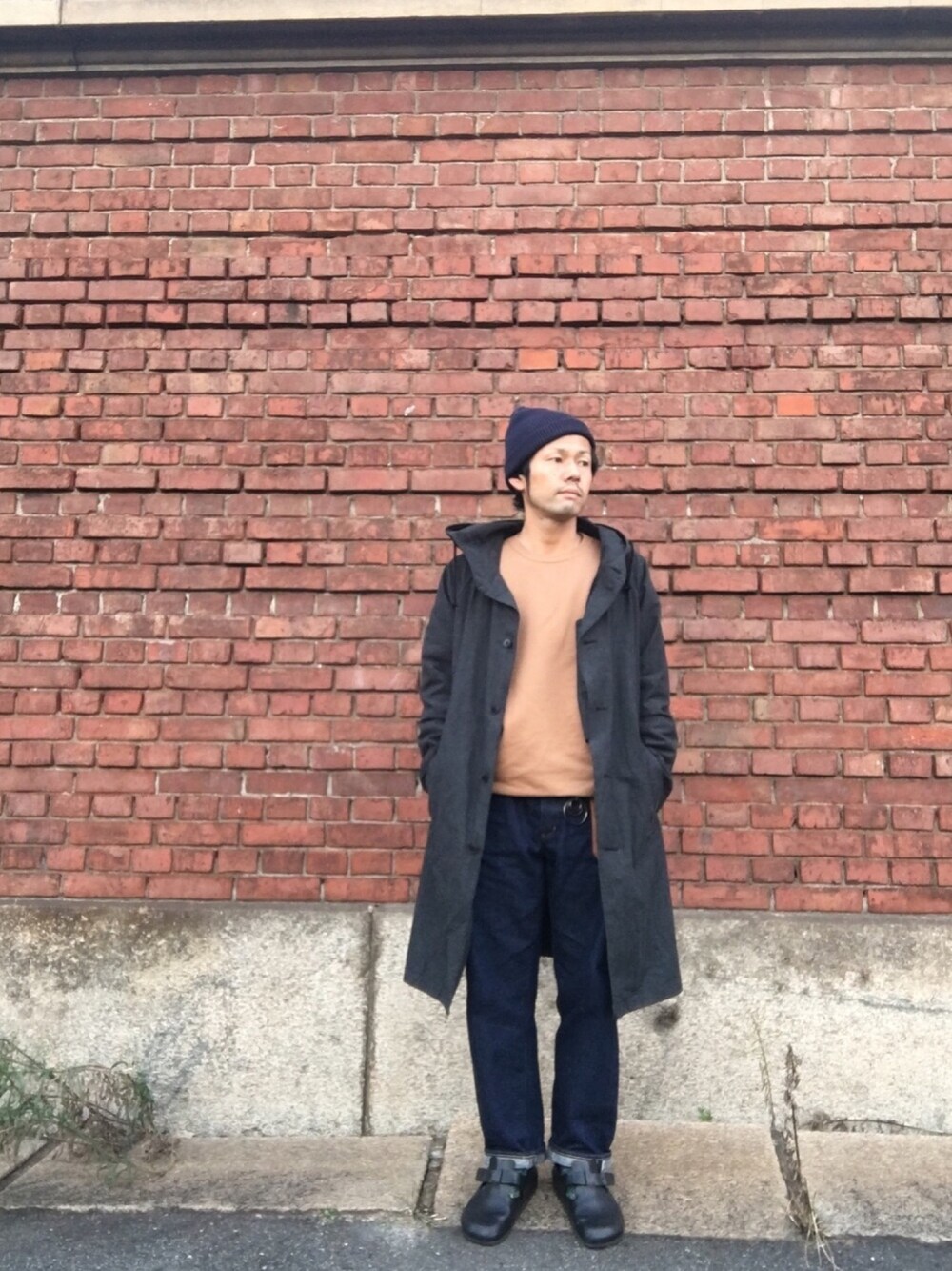 ブラック系のステンカラーコート、ベージュ系のスウェット、ブルー系のデニムパンツを着用したメンズの秋コーディネートの1枚目の写真