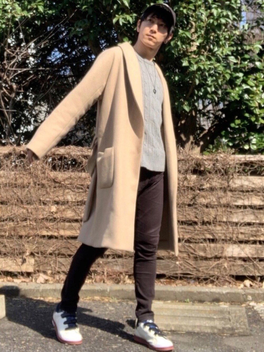 ベージュ系のチェスターコート、グレー系のニット/セーター、ブラック系のデニムパンツを着用したメンズの春コーディネートの1枚目の写真
