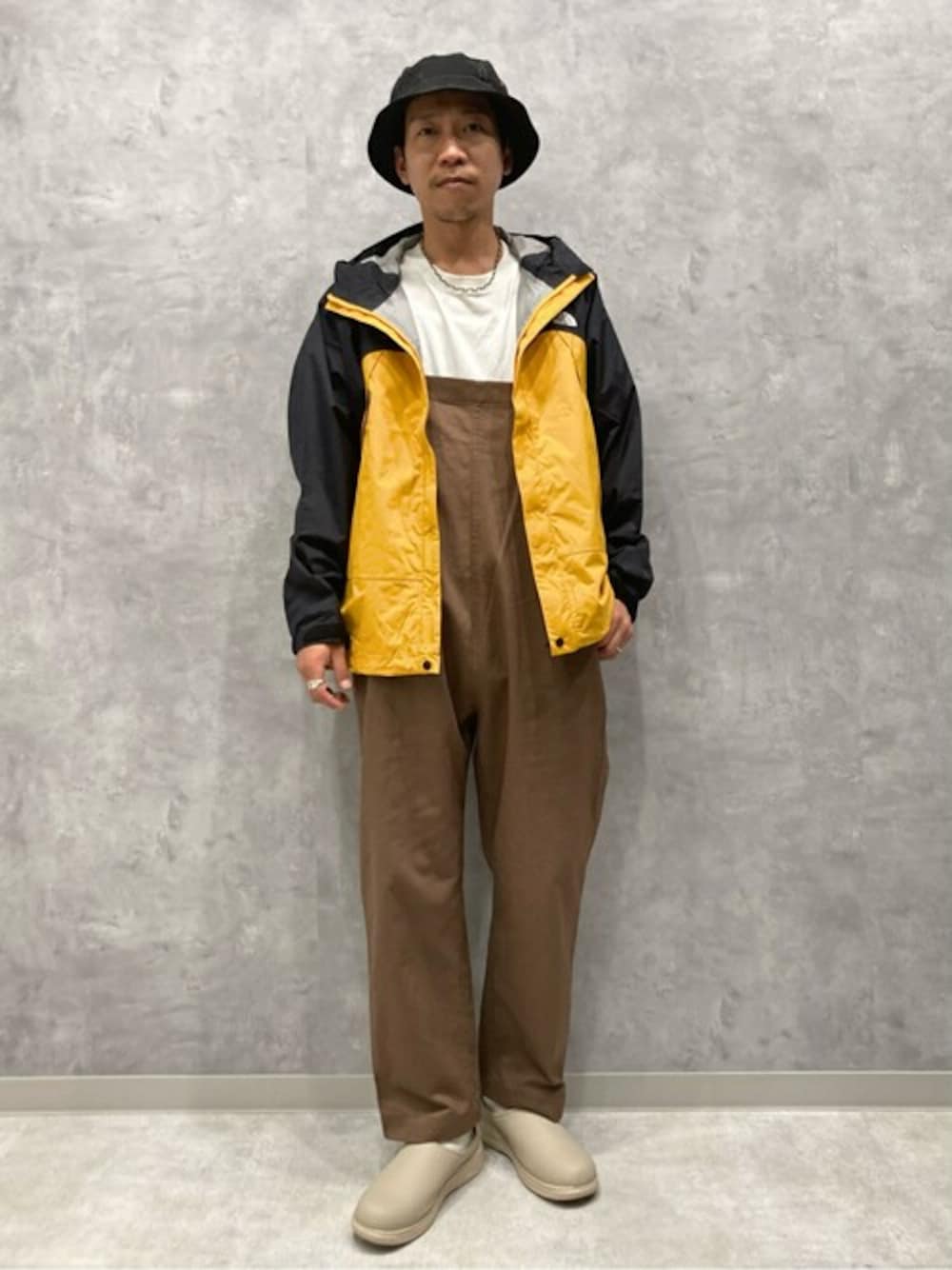 オレンジ系のマウンテンパーカー、ブラウン系のサロペット/オーバーオールを着用したメンズの春コーディネートの1枚目の写真
