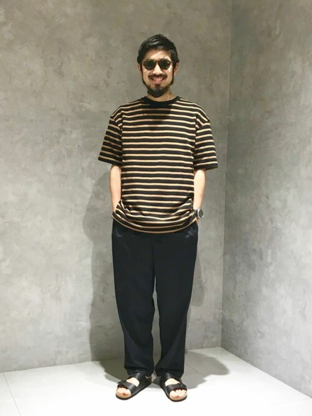 ブラック系のTシャツ/カットソー、ブルー系のスラックス、ブラック系のサンダルを着用したメンズの夏コーディネートの1枚目の写真