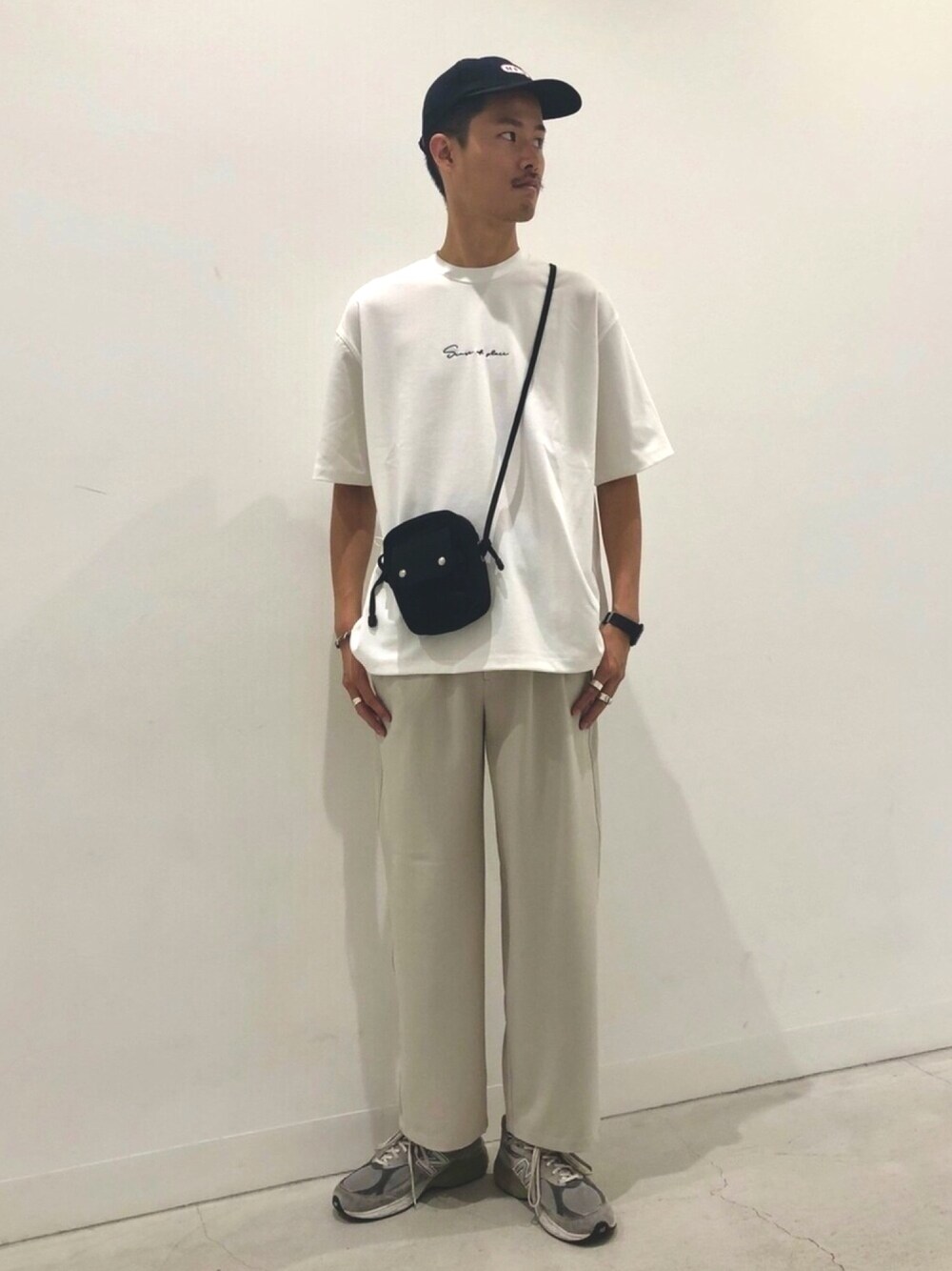 ホワイト系のTシャツ/カットソー、ブラック系のショルダーバッグ、ベージュ系のスラックスを着用したメンズの春コーディネートの1枚目の写真