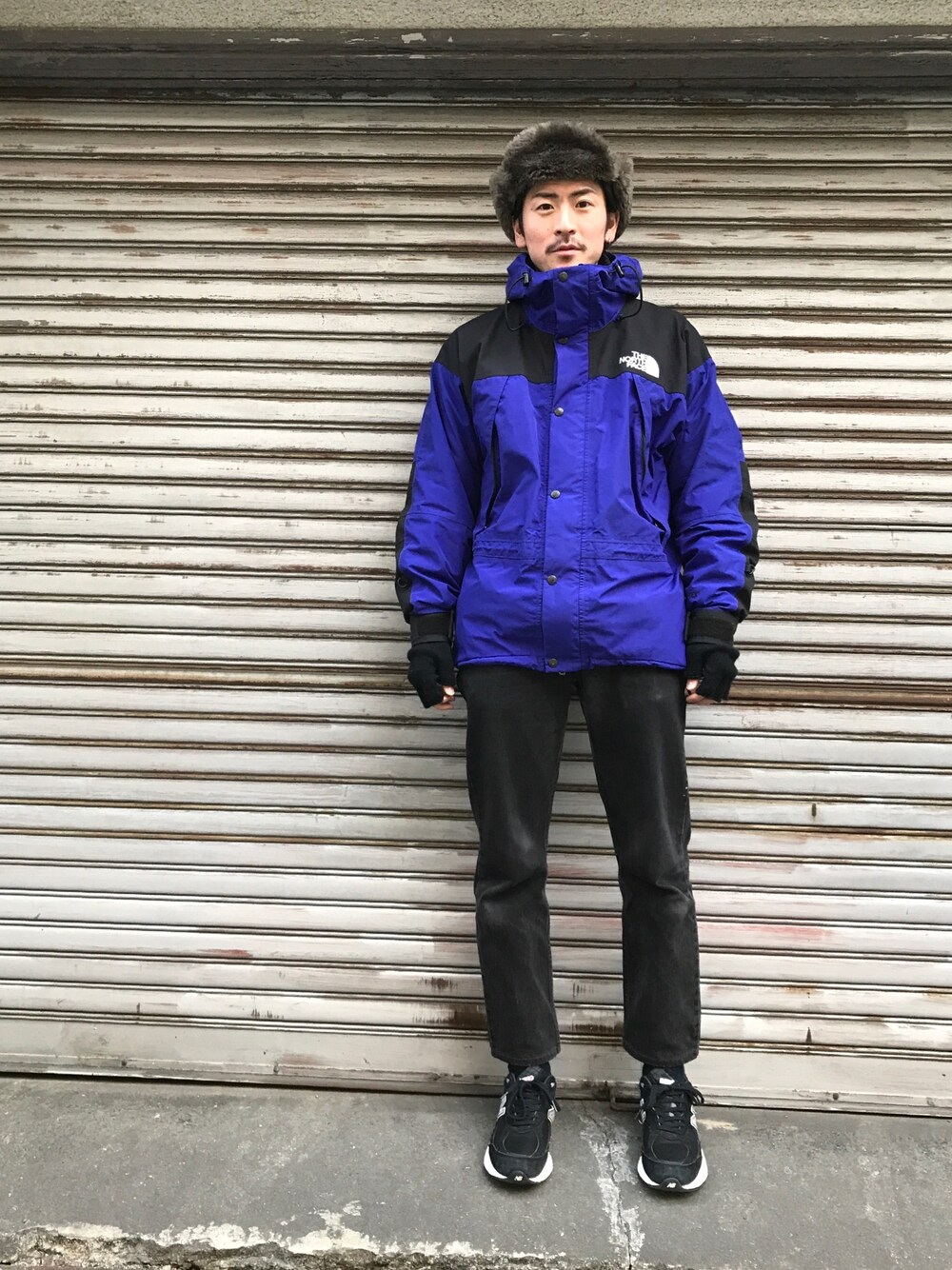 ブラック系のデニムパンツ、ブラック系のスニーカー、ブルー系のマウンテンパーカーを着用したメンズの冬コーディネートの1枚目の写真