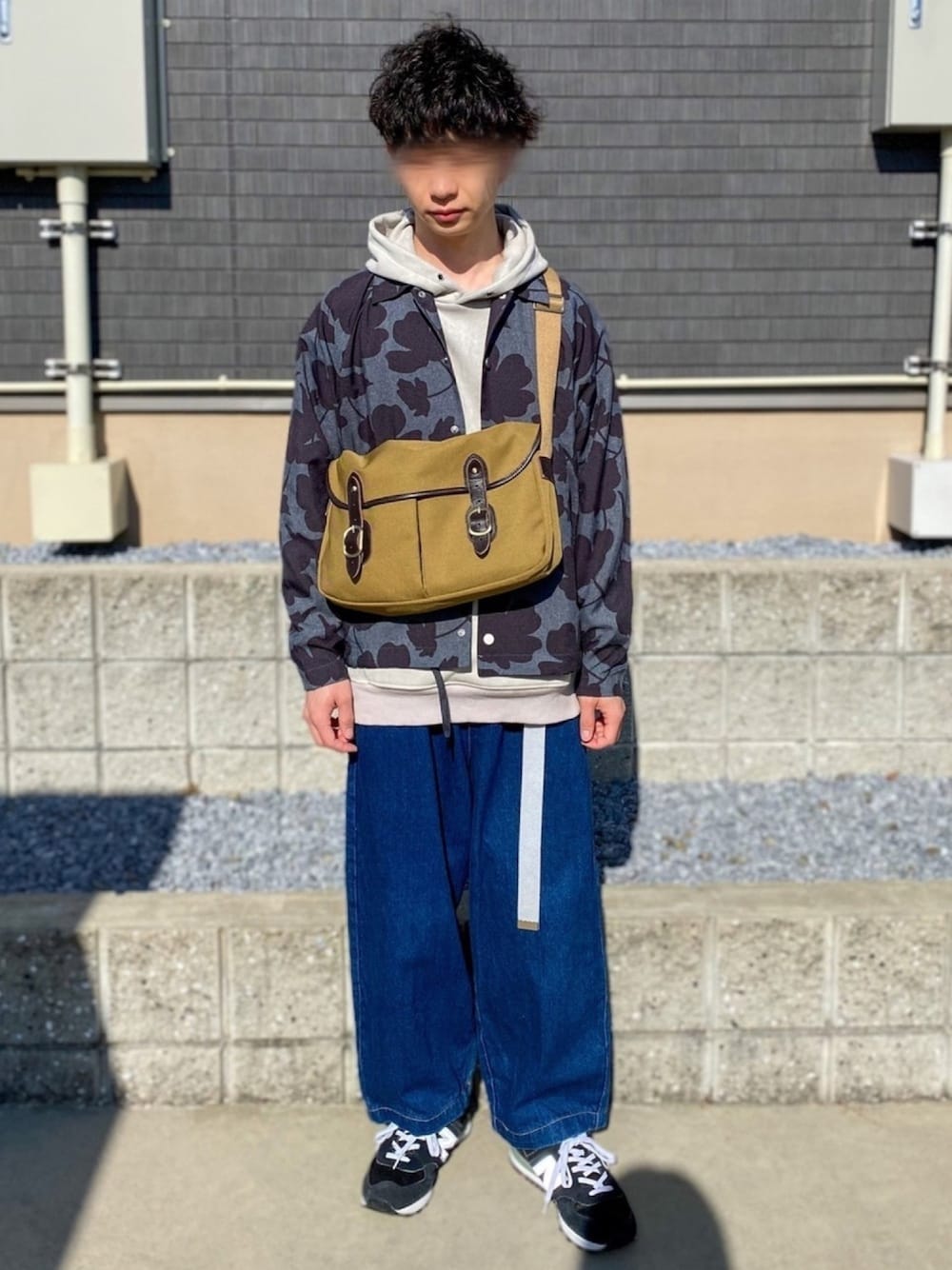 グレー系のパーカー、ベージュ系のショルダーバッグ、ブルー系のデニムパンツを着用したメンズの春コーディネートの1枚目の写真