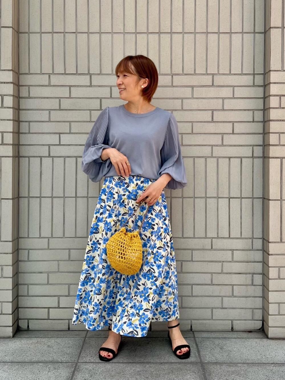 ブルー系のニット/セーター、イエロー系のハンドバッグ、ホワイト系のスカートを着用したレディースの春コーディネートの1枚目の写真