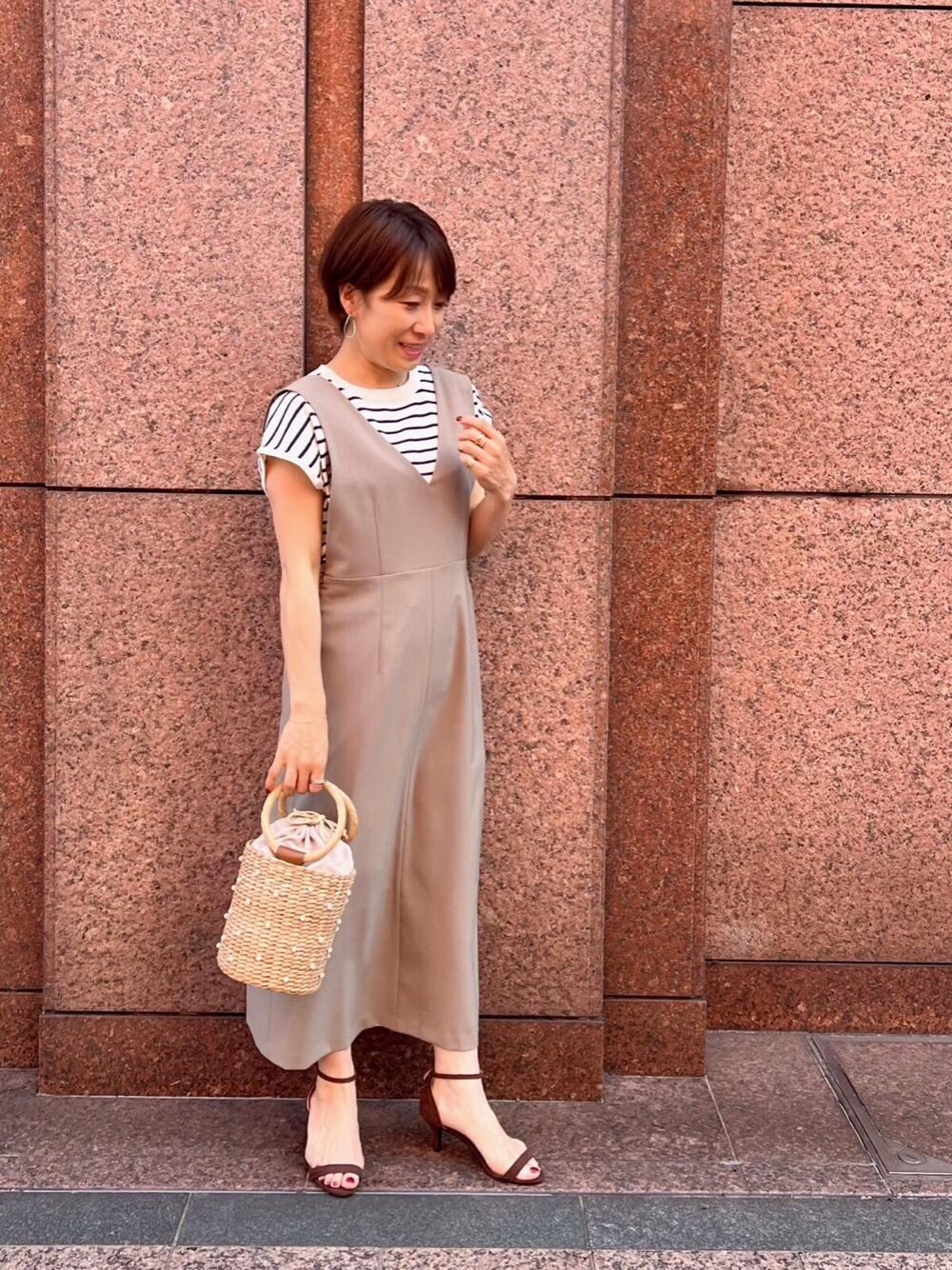 ベージュ系のかごバッグ、ホワイト系のニット/セーター、ブラウン系のジャンパースカートを着用したレディースの春コーディネートの1枚目の写真