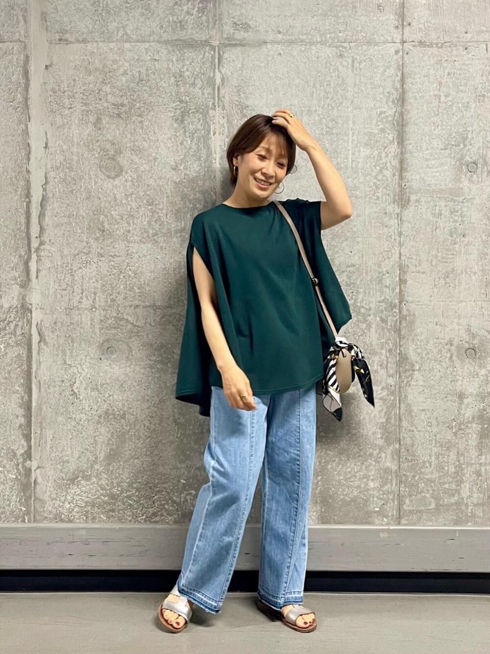 ベージュ系のショルダーバッグ、ブルー系のデニムパンツ、グリーン系のニット/セーターを着用したレディースの夏コーディネートの1枚目の写真