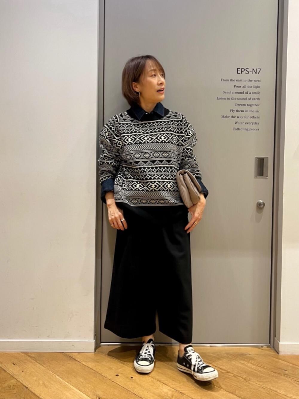 ブラック系のスラックス、ブラック系のニット/セーター、ブルー系のシャツ/ブラウスを着用したレディースの秋コーディネートの1枚目の写真