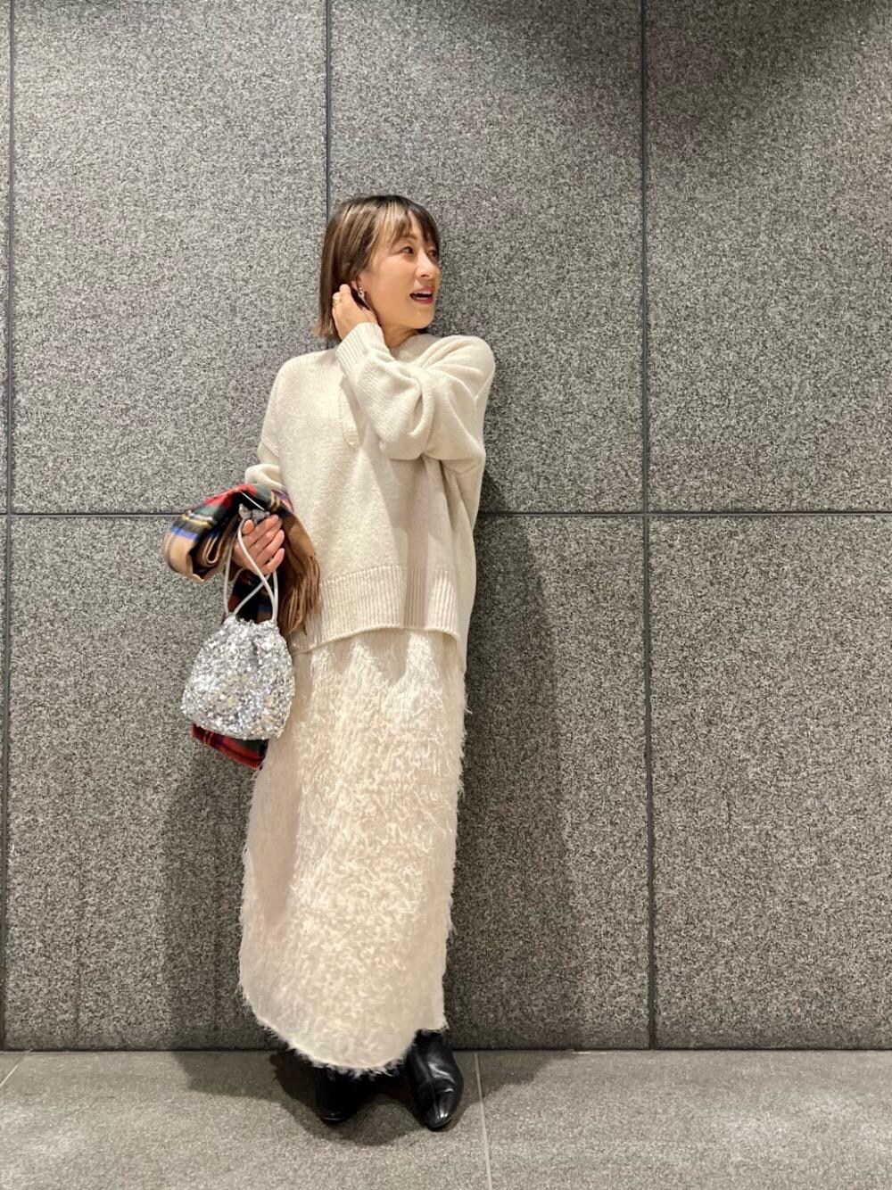 ベージュ系のニット/セーター、ホワイト系のスカート、ブラウン系のストール/ショールを着用したレディースの秋コーディネートの1枚目の写真