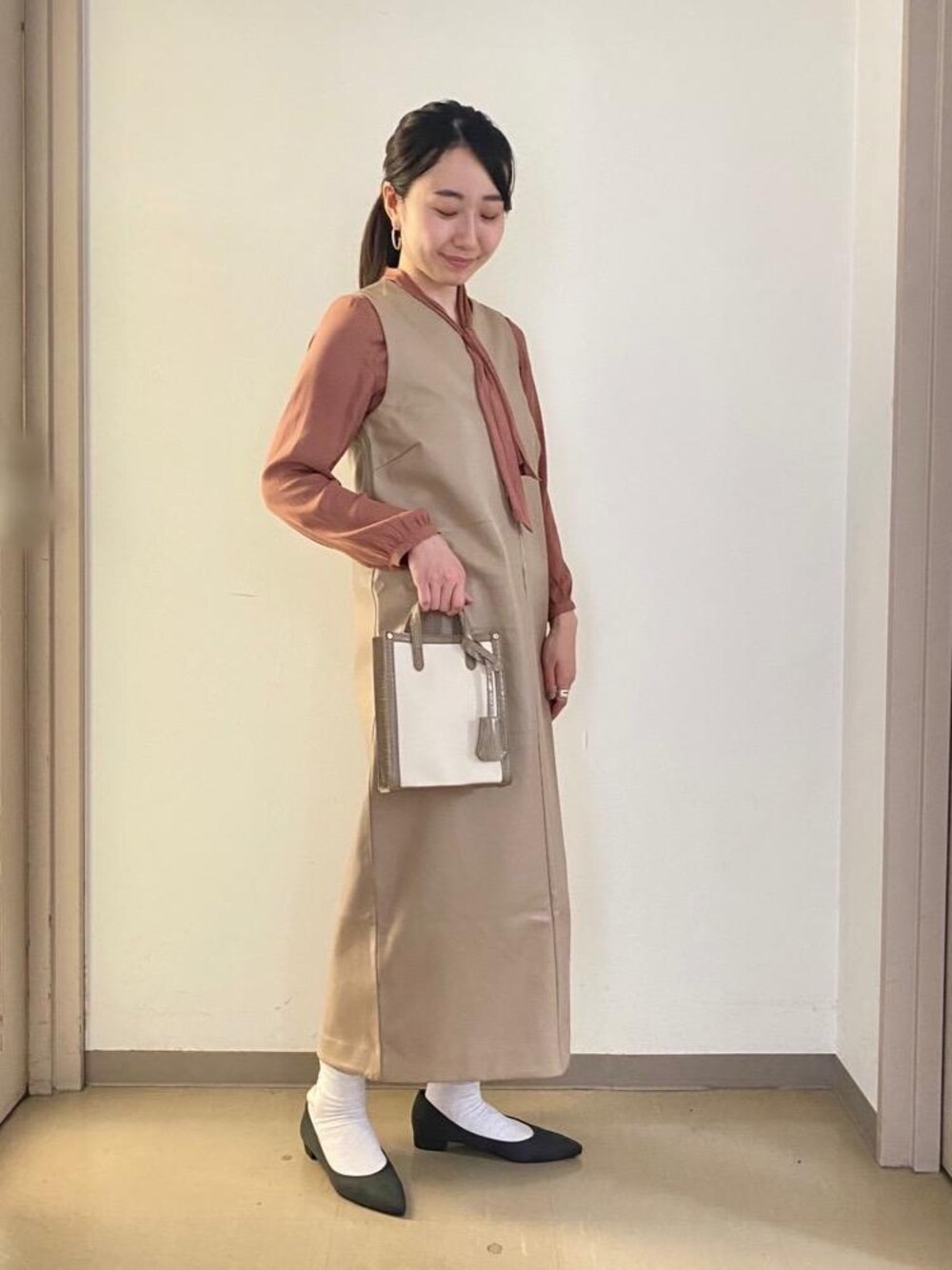 ベージュ系のショルダーバッグ、ベージュ系のジャンパースカート、グレー系のパンプスを着用したレディースの秋コーディネートの1枚目の写真