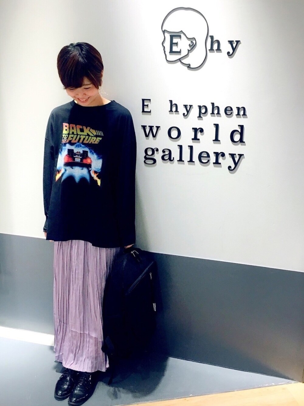 ブラック系のトートバッグ、パープル系のスカート、ブラック系のTシャツ/カットソーを着用したレディースの秋コーディネートの1枚目の写真
