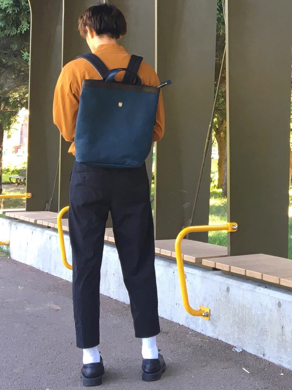 オレンジ系のTシャツ/カットソー、ブルー系のバックパック/リュック、ブラック系のスラックスを着用したメンズの秋コーディネートの1枚目の写真