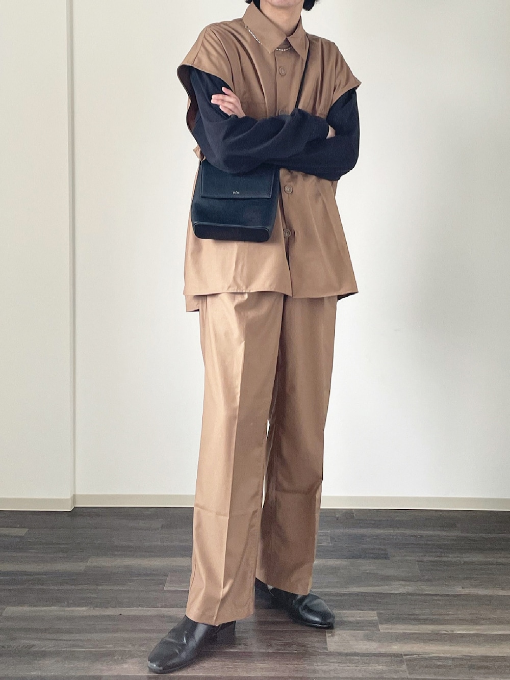 ブラウン系のベスト、ブラウン系のスラックス、ブラック系のショルダーバッグを着用したメンズの春コーディネートの1枚目の写真