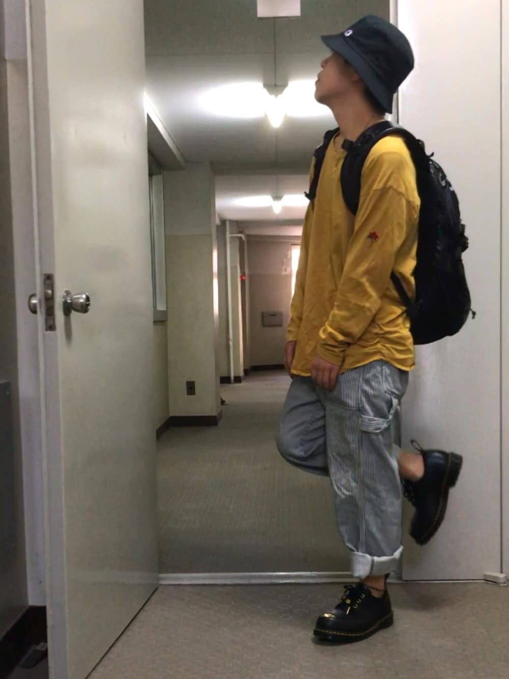 「イエロー、ストライプパンツ、Dr.Martens、ロンT、黒リュック、バケットハット、ヒッコリーパンツ、ワイドパンツ、ワイドデニム、ロールアップ」｜「Championの【Champion】バケットハット（ハット、ブラック系）」を使った、むっくさん（メンズ・159cm）の春コーディネートの1枚目の写真