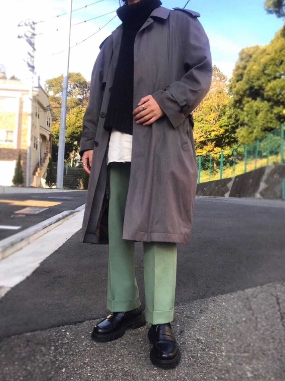グレー系のステンカラーコート、グリーン系のスラックス、ブラック系のローファーを着用したメンズの冬コーディネートの1枚目の写真