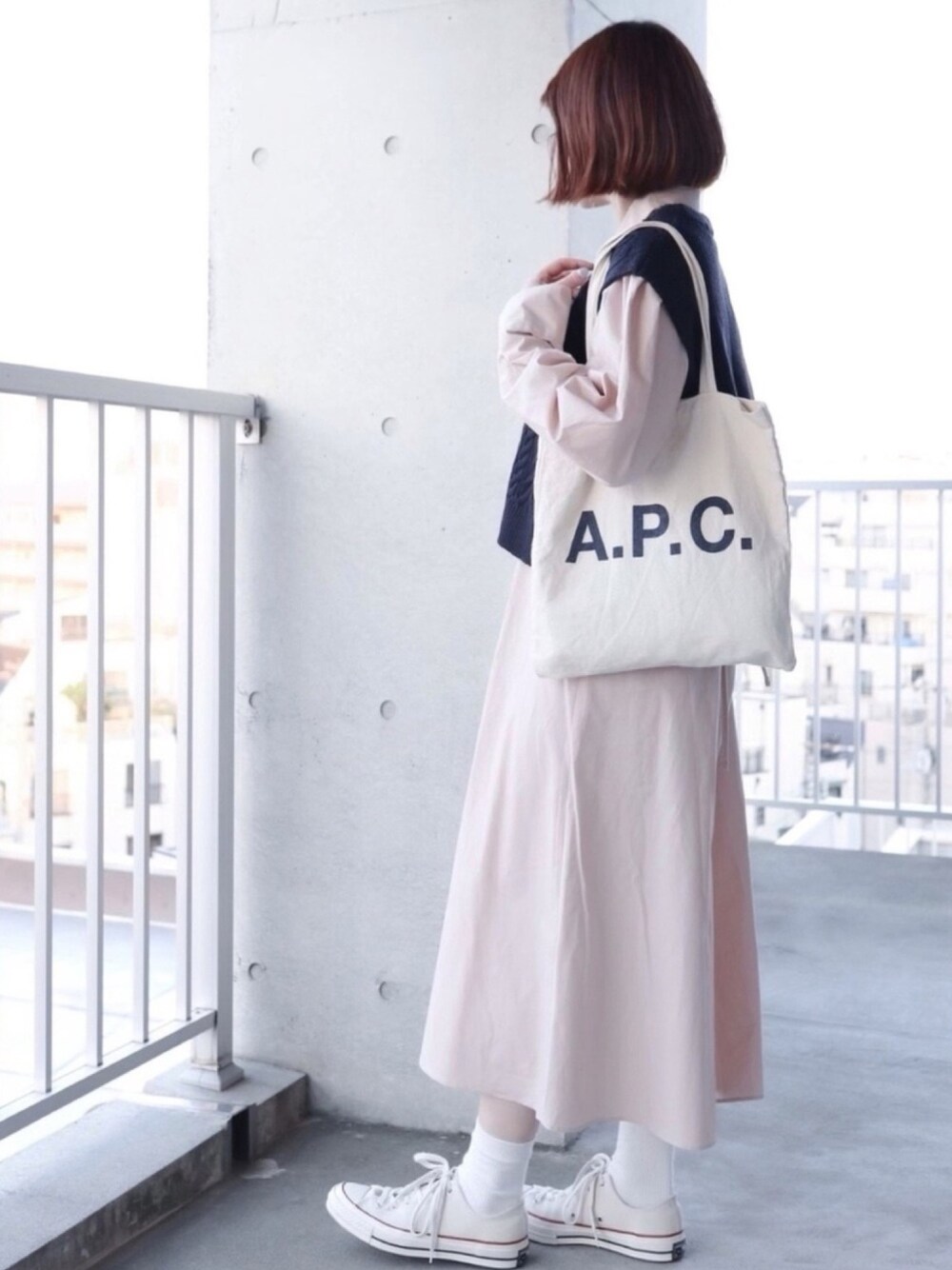 ピンク系のシャツワンピース、ブルー系のベスト、ホワイト系のスニーカーを着用したレディースの春コーディネートの1枚目の写真
