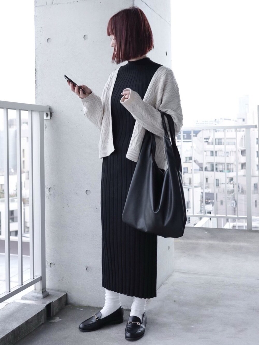 ブラック系のワンピース、ホワイト系のカーディガン/ボレロ、ブラック系のトートバッグを着用したレディースの冬コーディネートの1枚目の写真