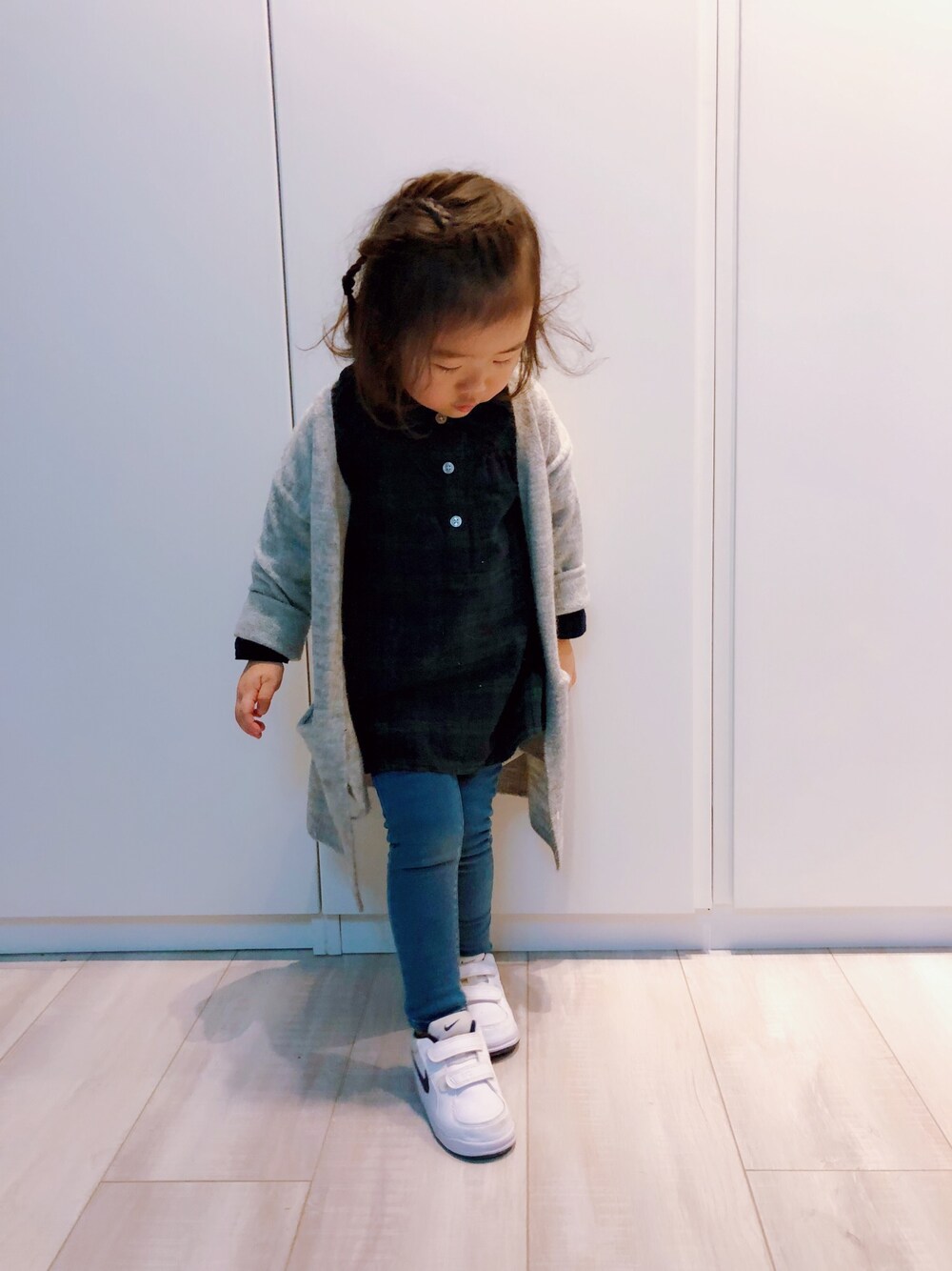 グリーン系のシャツワンピース、グレー系のカーディガン/ボレロ、ブルー系のデニムパンツを着用したキッズの冬コーディネートの1枚目の写真