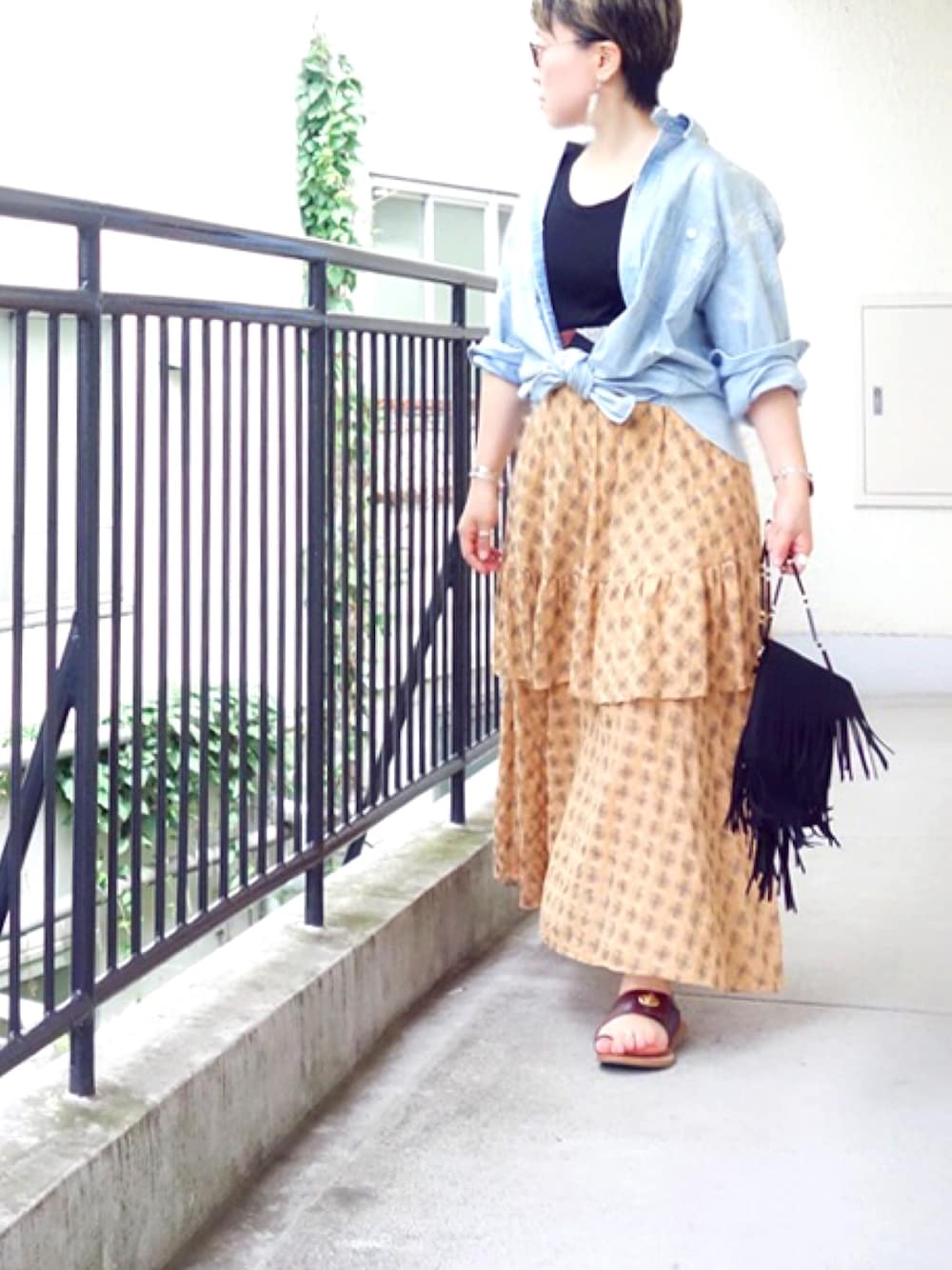 オレンジ系のスカート、ブラウン系のシューズ、ブラック系のショルダーバッグを着用したレディースの夏コーディネートの1枚目の写真