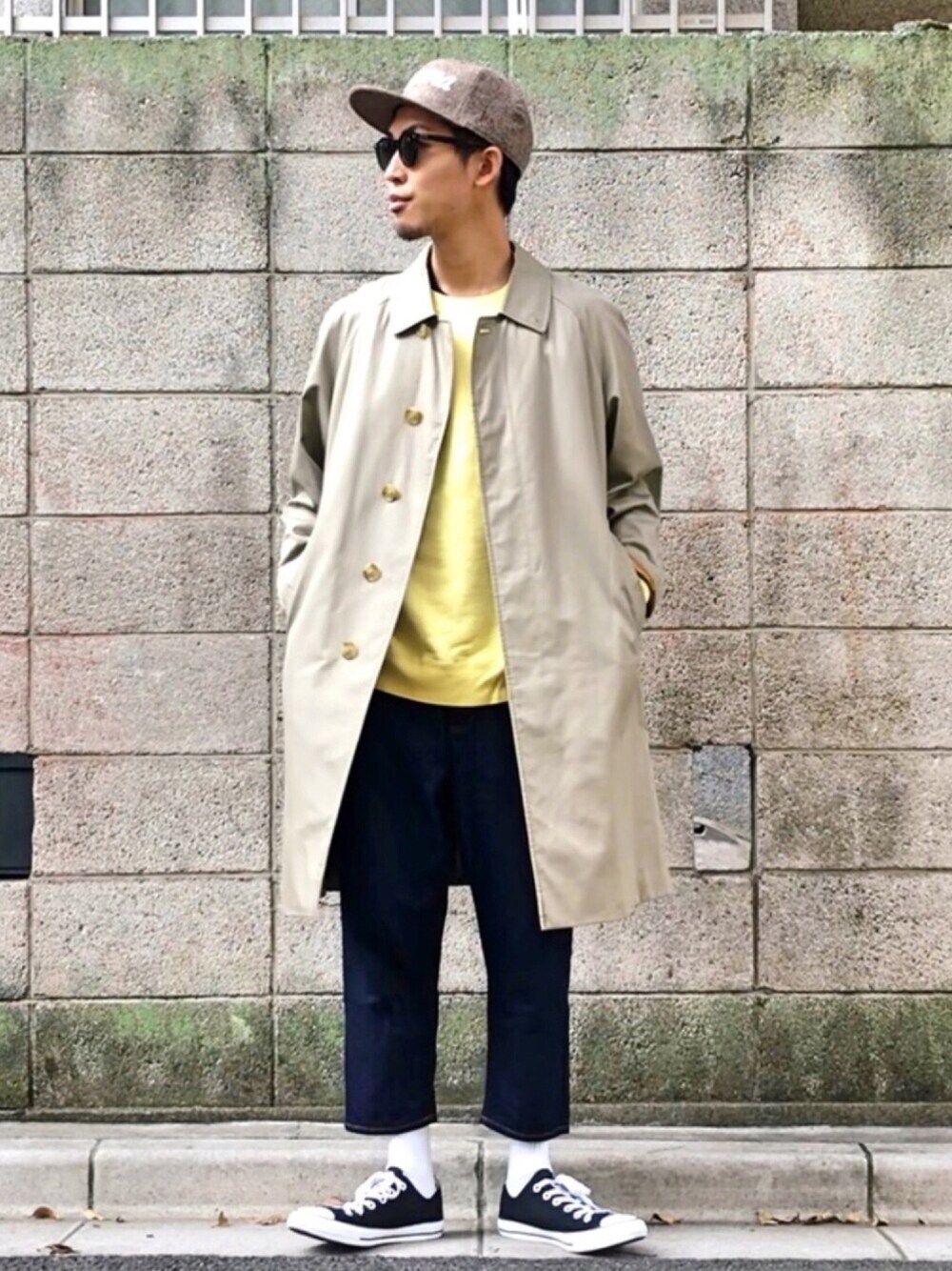 ベージュ系のステンカラーコート、イエロー系のTシャツ/カットソー、ブルー系のデニムパンツを着用したメンズの秋コーディネートの1枚目の写真