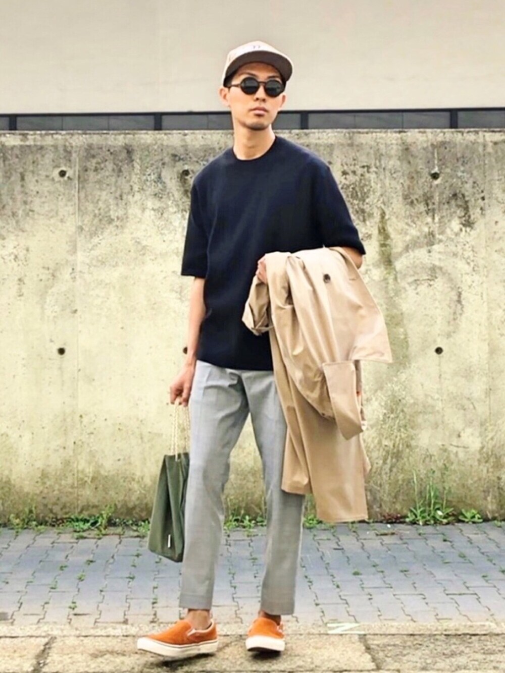 ブラック系のニット/セーター、ベージュ系のトレンチコート、グレー系のパンツを着用したメンズの春コーディネートの1枚目の写真
