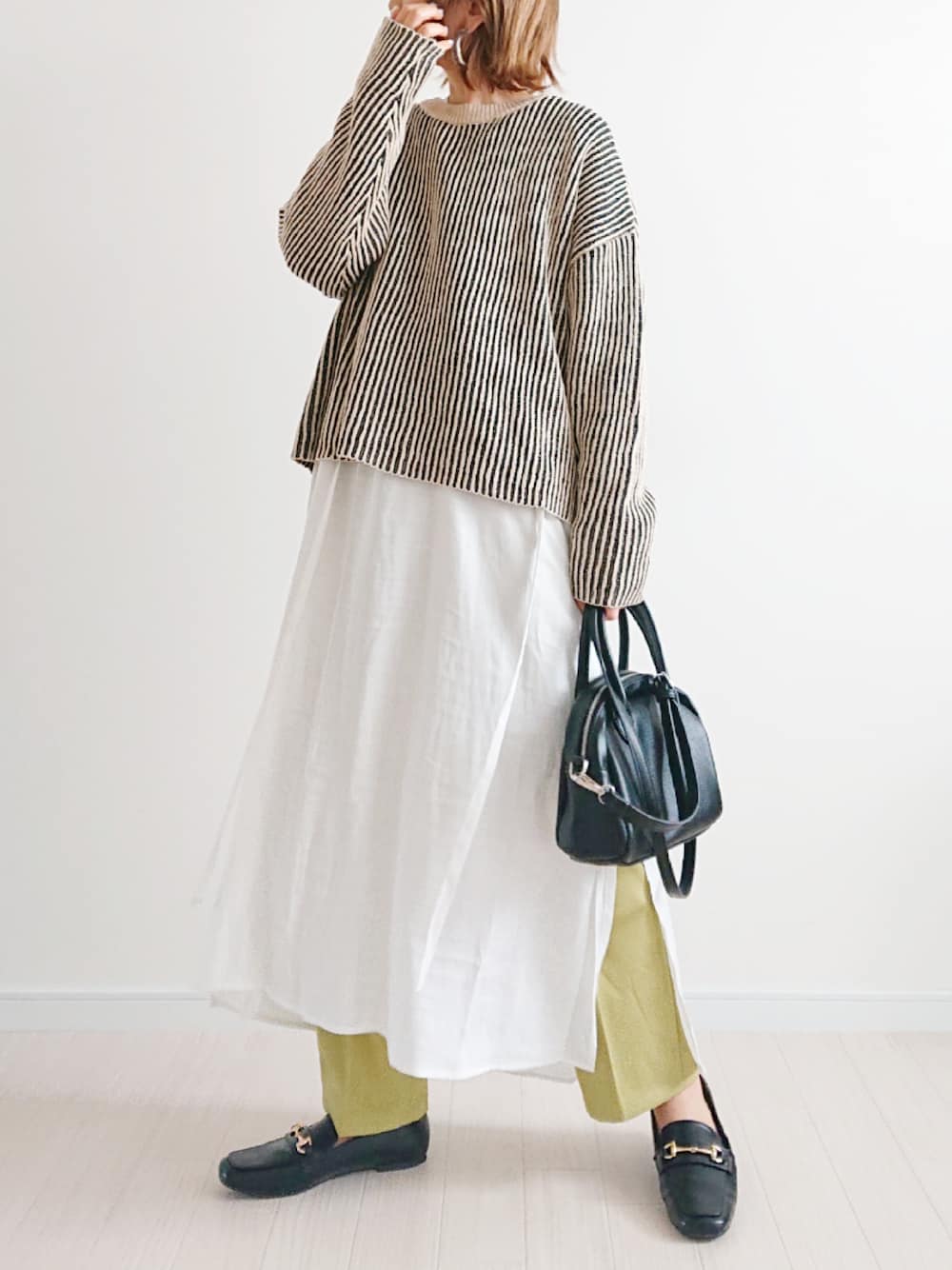 ホワイト系のシャツワンピース、ブラック系のニット/セーター、ブラック系のローファーを着用したレディースの春コーディネートの1枚目の写真