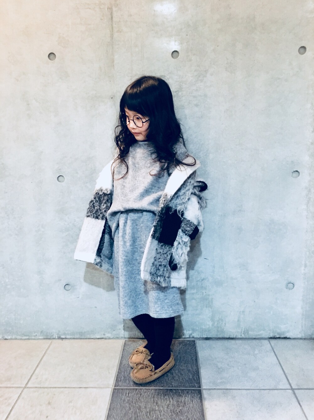 グレー系のスカート、グレー系のチェスターコート、ベージュ系のモカシン/デッキシューズを着用したキッズの秋コーディネートの1枚目の写真