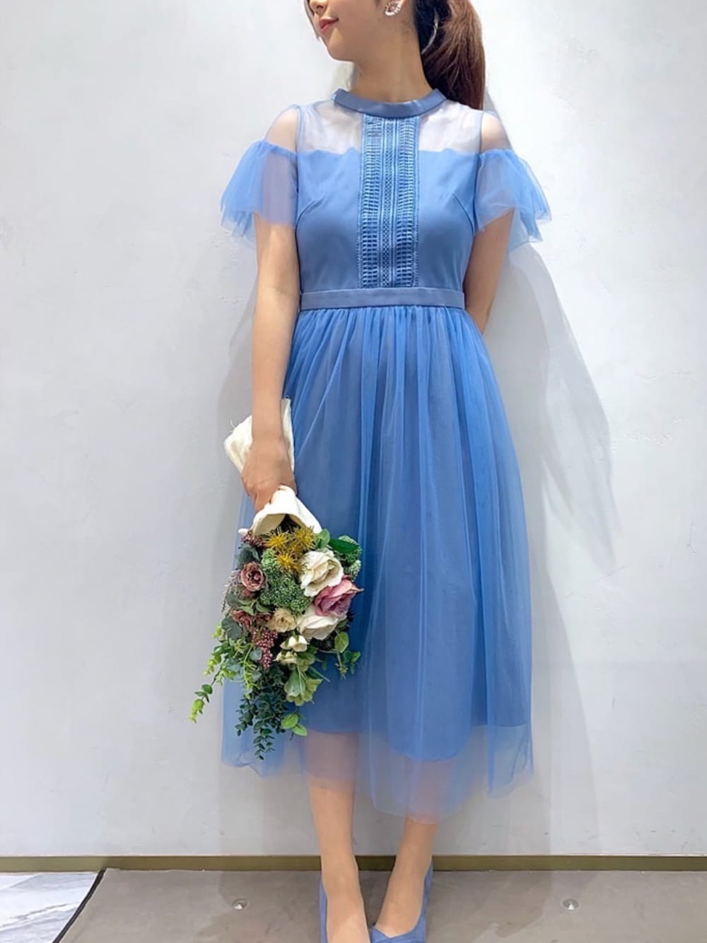 ブルー系のドレス、グレー系のパンプス、ゴールド系のイヤリングを着用したレディースの冬コーディネートの1枚目の写真