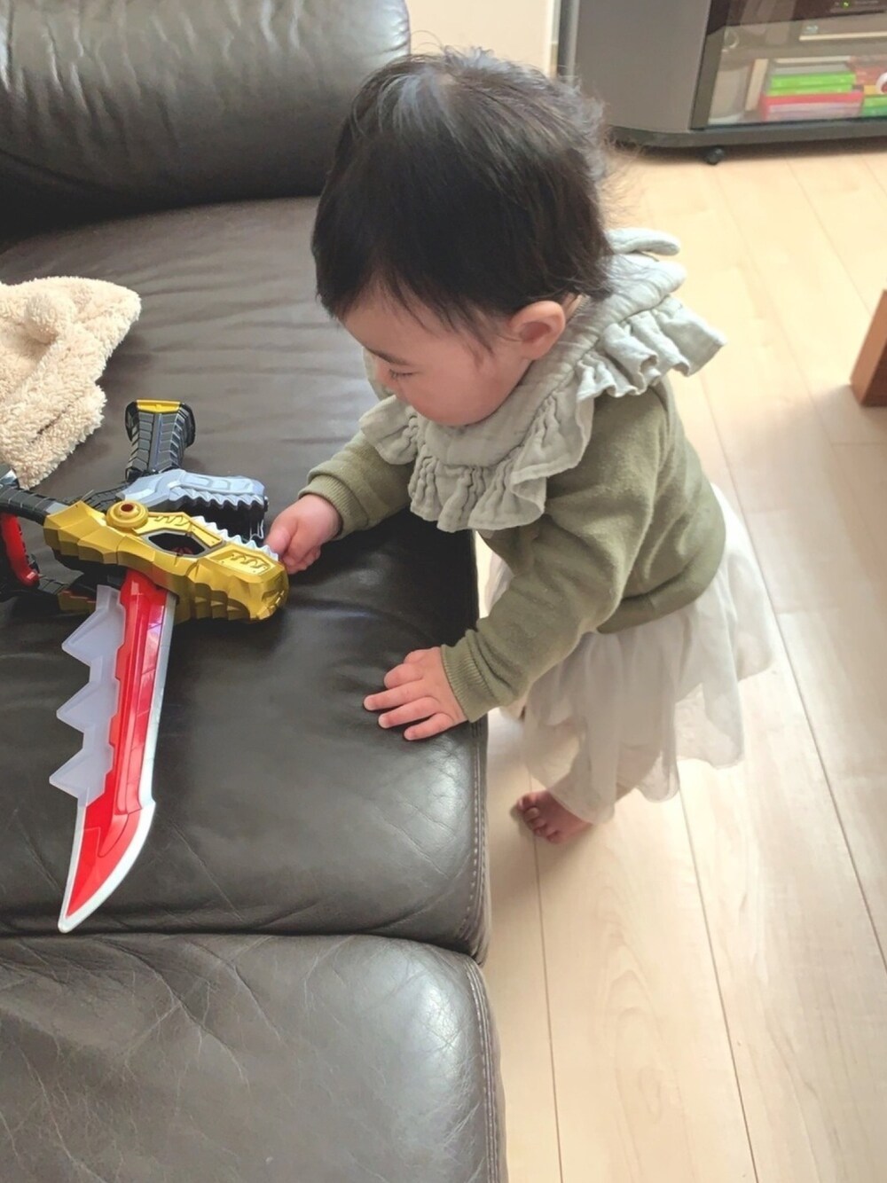 グリーン系のトップス、グリーン系のスタイ/よだれかけ、レッド系のおもちゃを着用したキッズの冬コーディネートの1枚目の写真