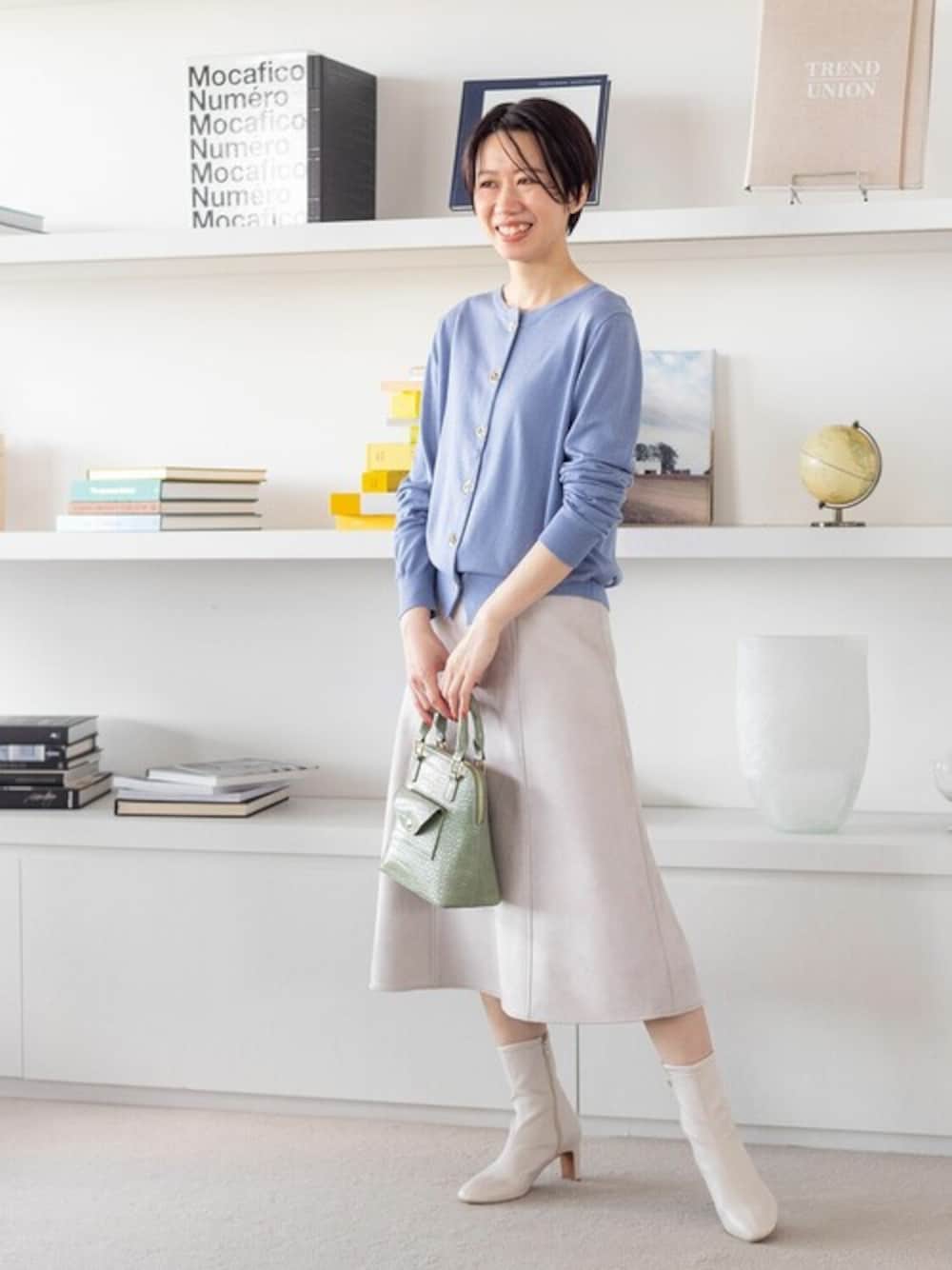 ブルー系のカーディガン/ボレロ、ベージュ系のスカート、グリーン系のハンドバッグを着用したレディースの秋コーディネートの1枚目の写真