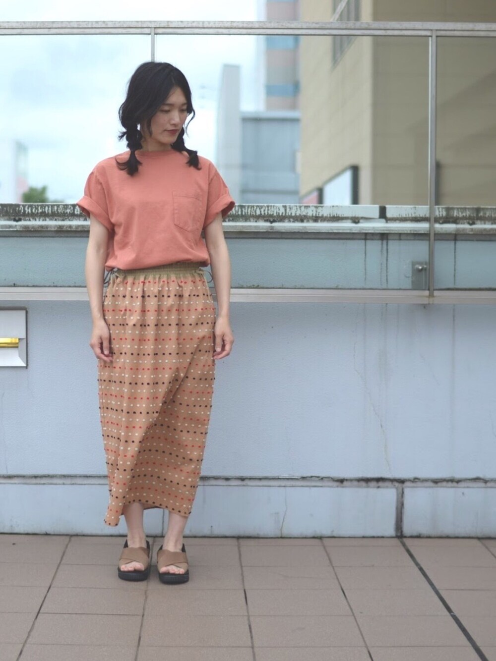 オレンジ系のTシャツ/カットソー、ベージュ系のスカート、ブラウン系のサンダルを着用したレディースの秋コーディネートの1枚目の写真
