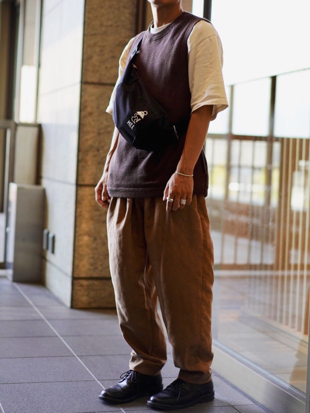 ブラウン系のベスト、ブラウン系のTシャツ/カットソー、ベージュ系のスラックスを着用したメンズの秋コーディネートの1枚目の写真