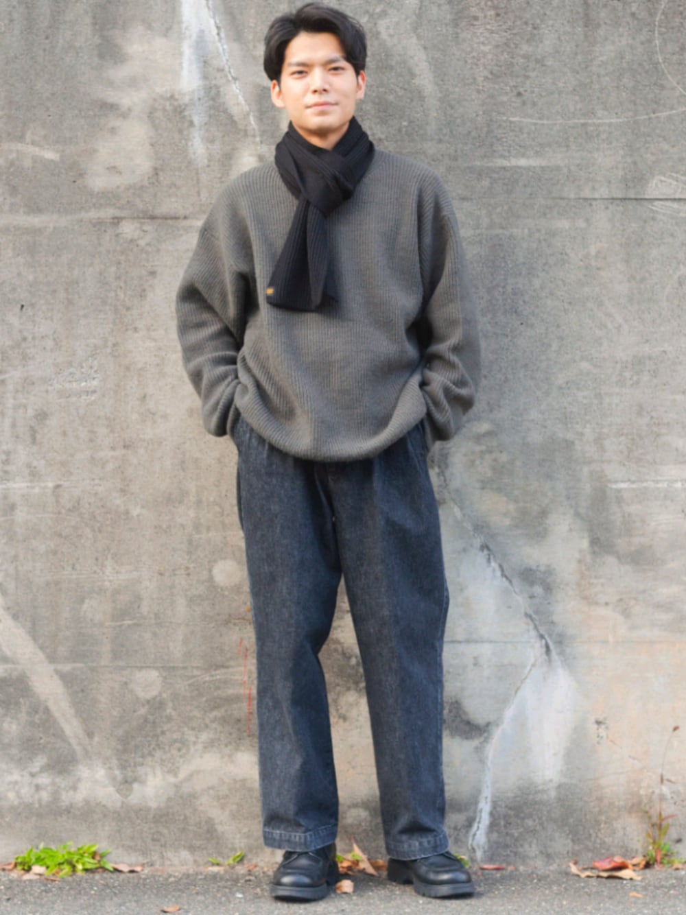 グレー系のデニムパンツ、グリーン系のニット/セーター、ブラック系のドレスシューズを着用したメンズの冬コーディネートの1枚目の写真