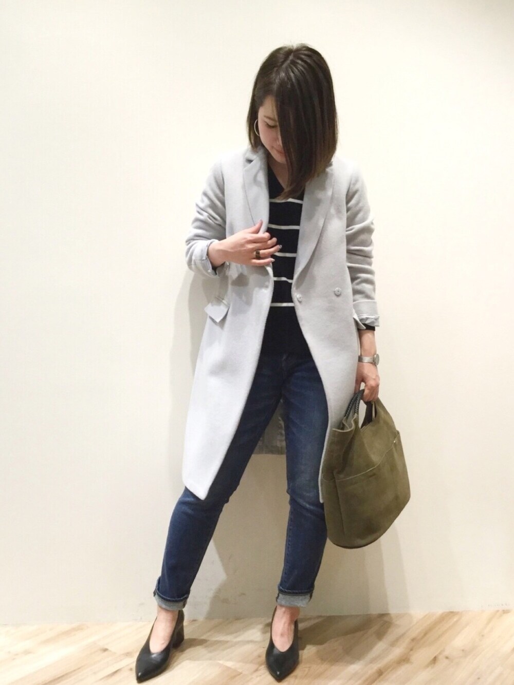 グリーン系のバッグ、グレー系のチェスターコート、ブルー系のデニムパンツを着用したレディースの秋コーディネートの1枚目の写真