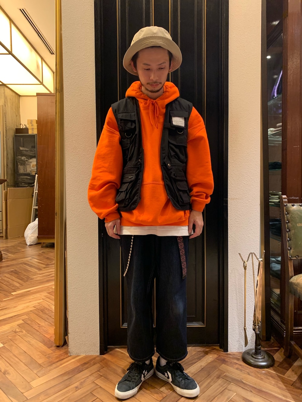 ブラック系のベスト、オレンジ系のパーカー、ブルー系のデニムパンツを着用したメンズの冬コーディネートの1枚目の写真