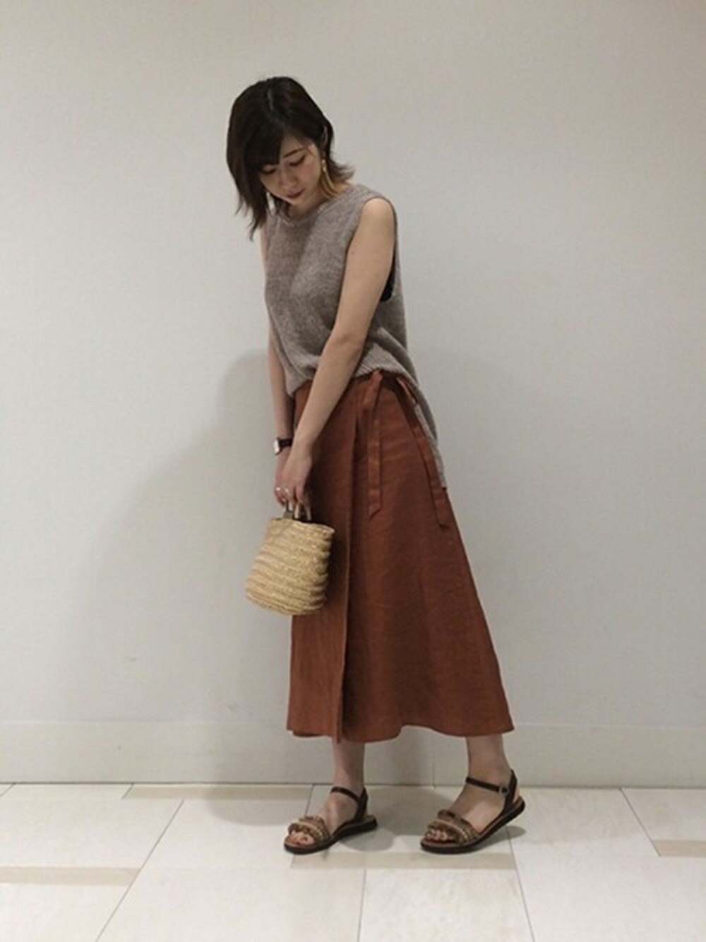 ベージュ系のベスト、レッド系のスカート、ゴールド系のトートバッグを着用したレディースの夏コーディネートの1枚目の写真
