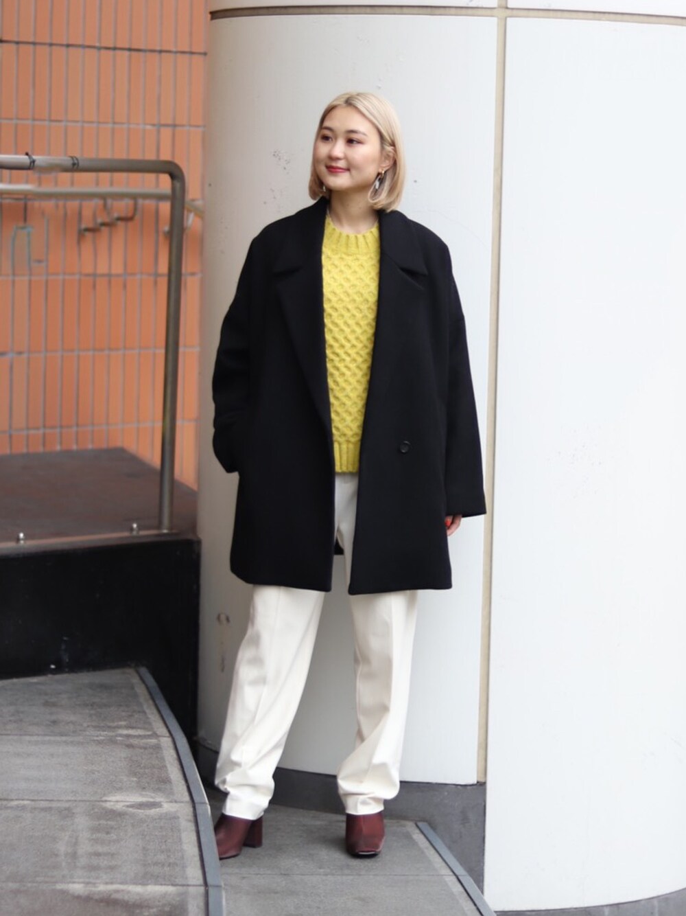 ブラック系のジャケット/アウター、イエロー系のニット/セーター、ホワイト系のスラックスを着用したレディースの冬コーディネートの1枚目の写真