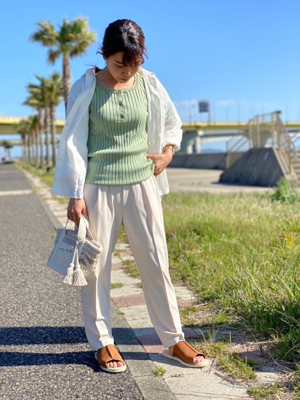 グリーン系のニット/セーター、ホワイト系のシャツ/ブラウス、ホワイト系のスラックスを着用したレディースの春コーディネートの1枚目の写真