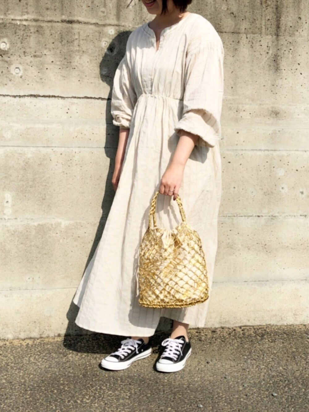 ゴールド系のトートバッグ、ホワイト系のワンピース、ブラック系のスニーカーを着用したレディースの春コーディネートの1枚目の写真