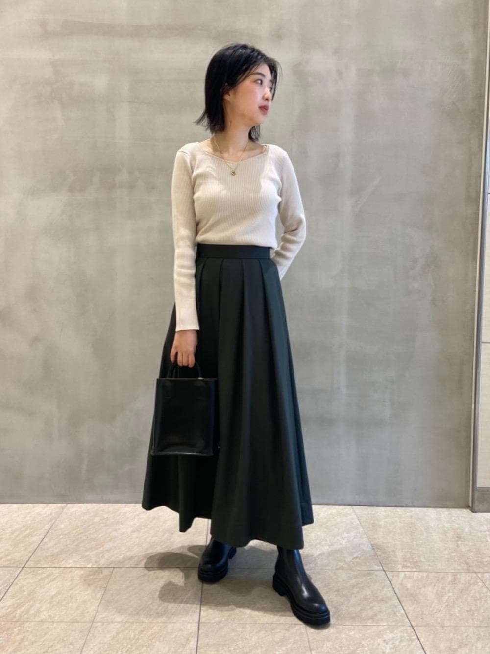 グレー系のスカート、ベージュ系のニット/セーター、ブラック系のブーツを着用したレディースの夏コーディネートの1枚目の写真