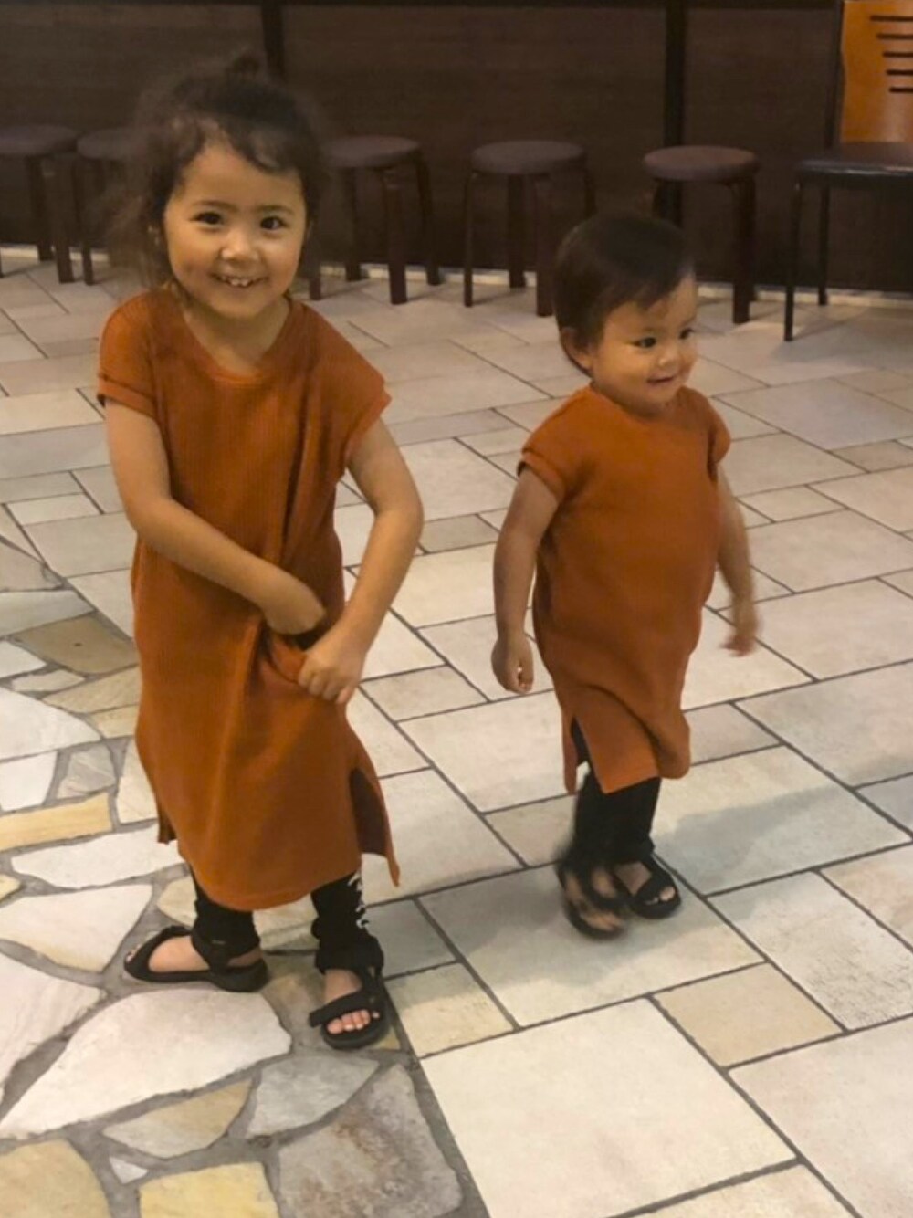 オレンジ系のワンピース/ドレス、ブラック系のスウェットパンツ、ブラック系のサンダルを着用したキッズの春コーディネートの1枚目の写真