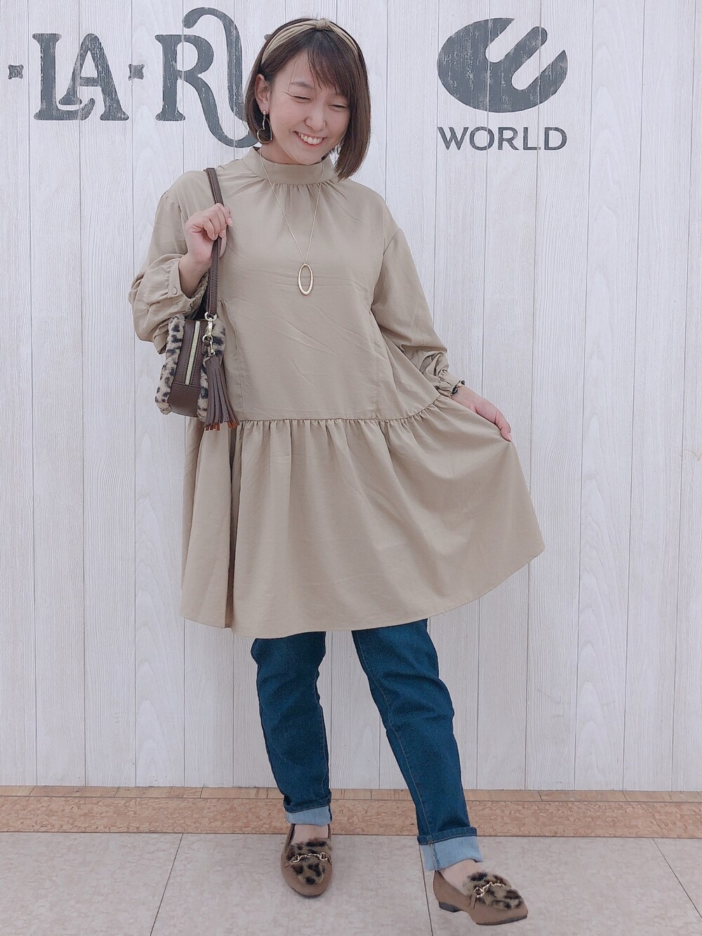 ベージュ系のチュニック、ブラウン系のショルダーバッグ、ブルー系のデニムパンツを着用したレディースの秋コーディネートの1枚目の写真