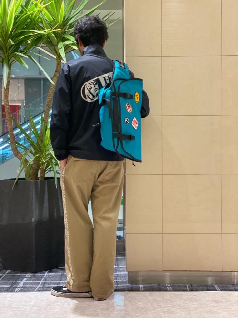 ベージュ系のその他パンツ、ブルー系のメッセンジャーバッグ、ブラック系のナイロンジャケットを着用したメンズの春コーディネートの1枚目の写真