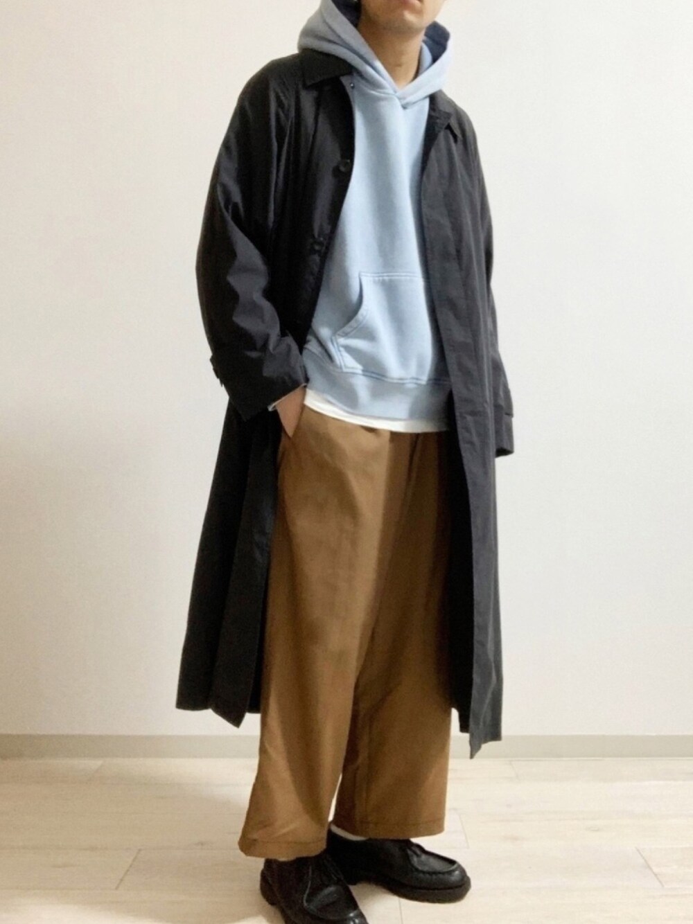 ブラック系のステンカラーコート、ブルー系のパーカー、ブラウン系のパンツを着用したメンズの春コーディネートの1枚目の写真
