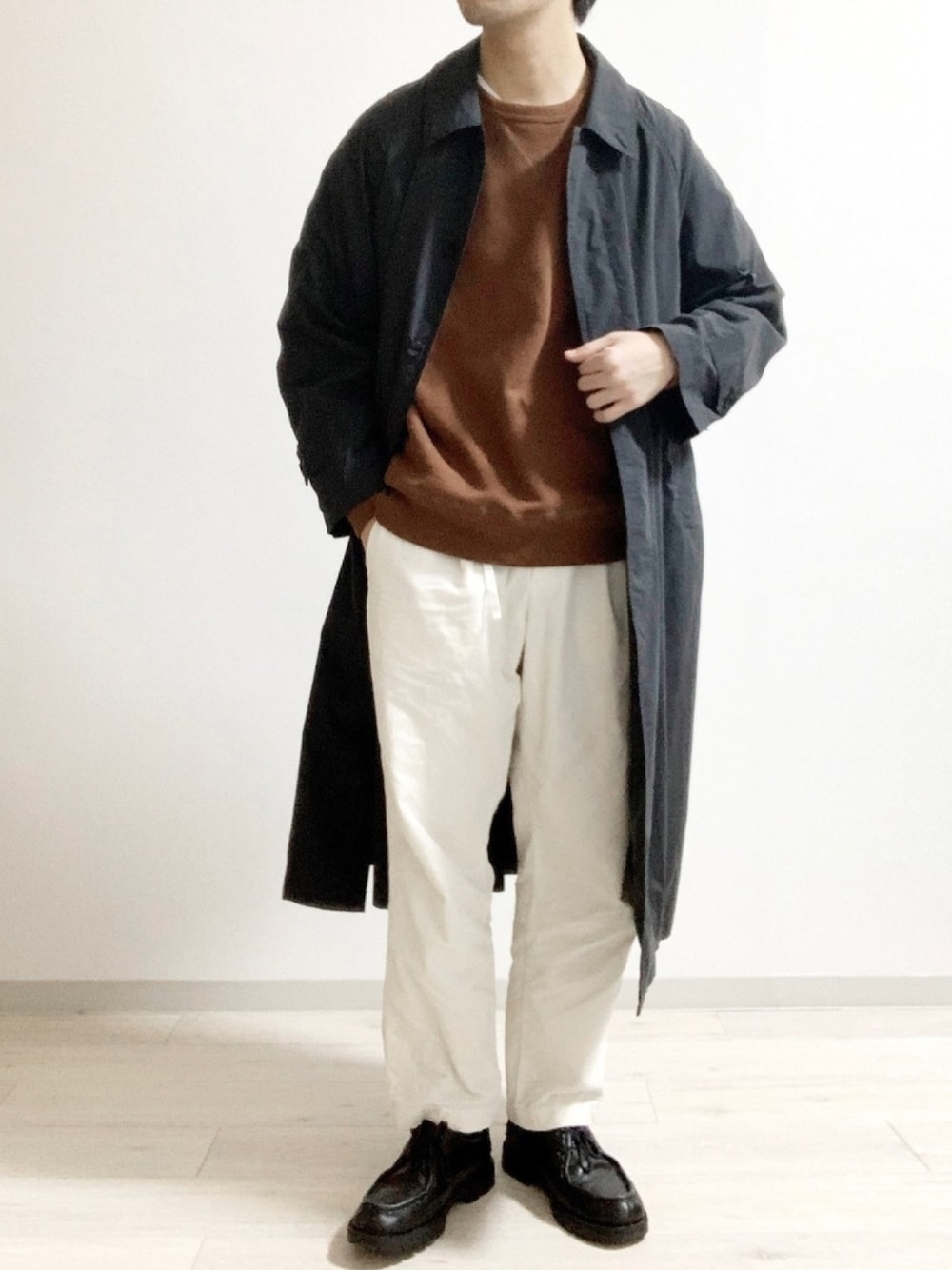 ブラック系のステンカラーコート、ブラウン系のスウェット、ホワイト系のその他パンツを着用したメンズの春コーディネートの1枚目の写真