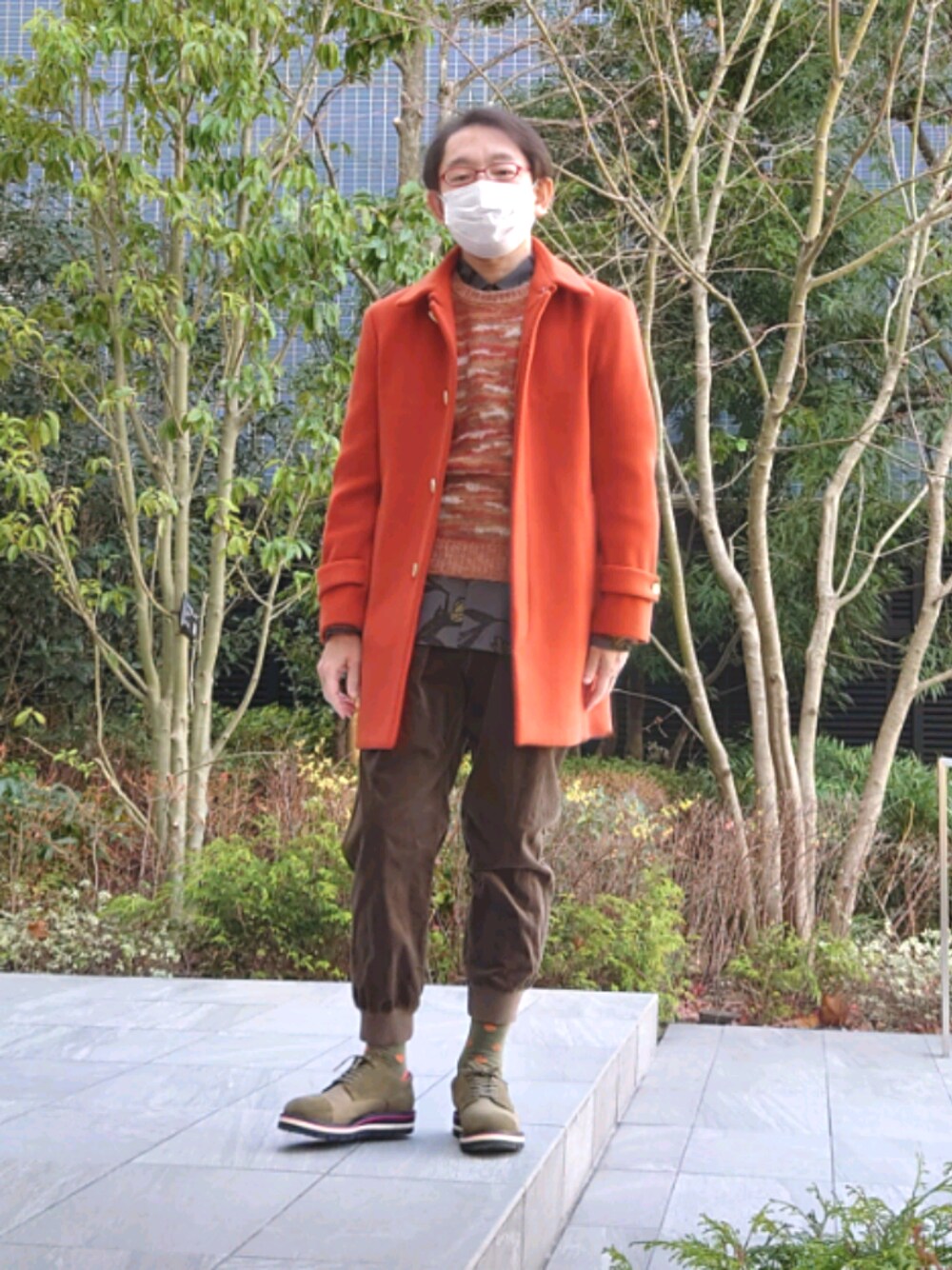 オレンジ系のニット/セーター、オレンジ系のステンカラーコート、ブラウン系のシャツ/ブラウスを着用したメンズの冬コーディネートの1枚目の写真