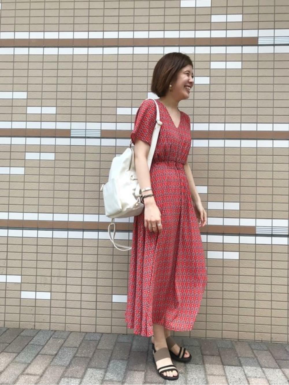 ホワイト系のバックパック/リュック、オレンジ系のワンピース、ホワイト系のイヤリングを着用したレディースの夏コーディネートの1枚目の写真