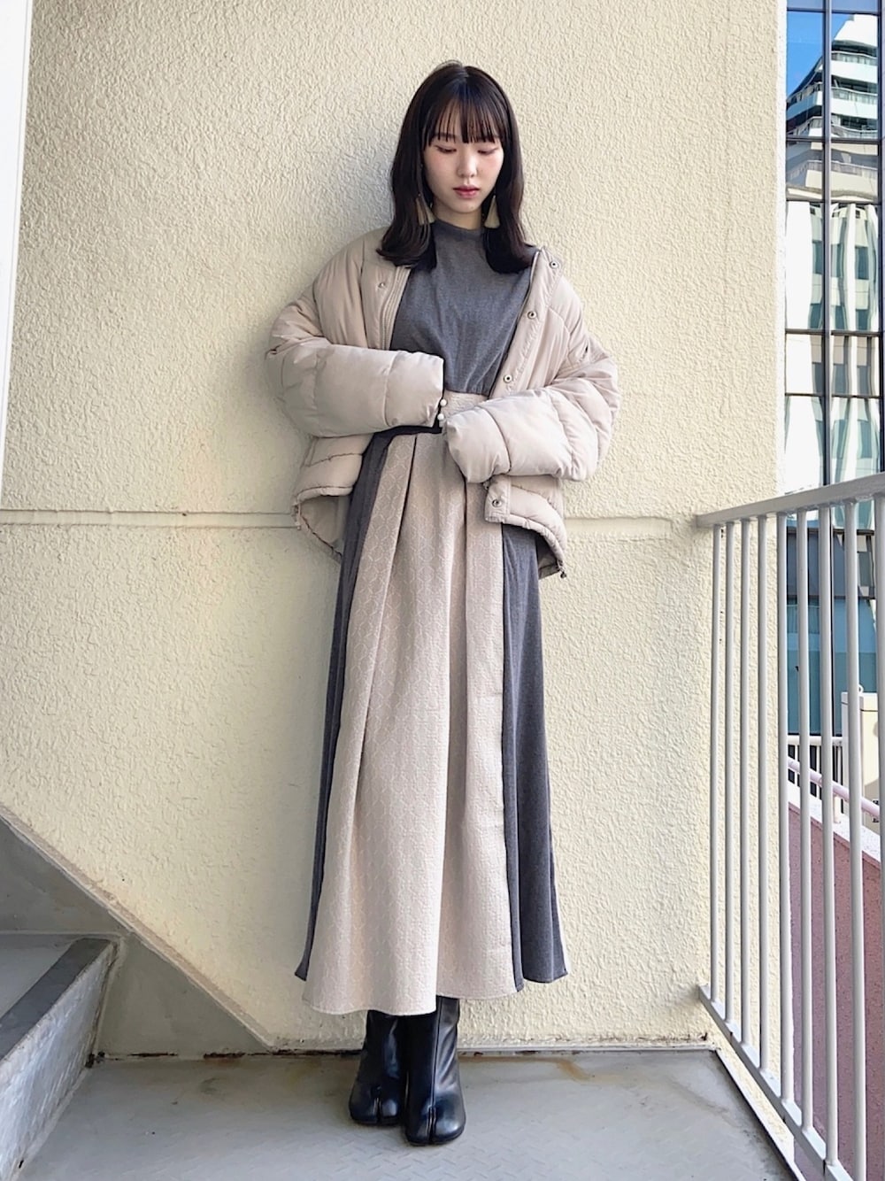 グレー系のノーカラーコート、グレー系のニット/セーター、グレー系のスカートを着用したレディースの秋コーディネートの1枚目の写真